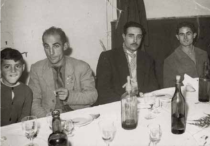 Francesc Moreno, Francesc Miró, Fèlix Sabaté i Ramon Giménez en una celebració de la colla a la primeria dels 60, probablement al local del Coro; al revers de la imatge hi ha aquestes curioses anotacions: número de mosquetón: 30.264, número de machete: 4.687; si en devia portar de mili aquesta fotografia!